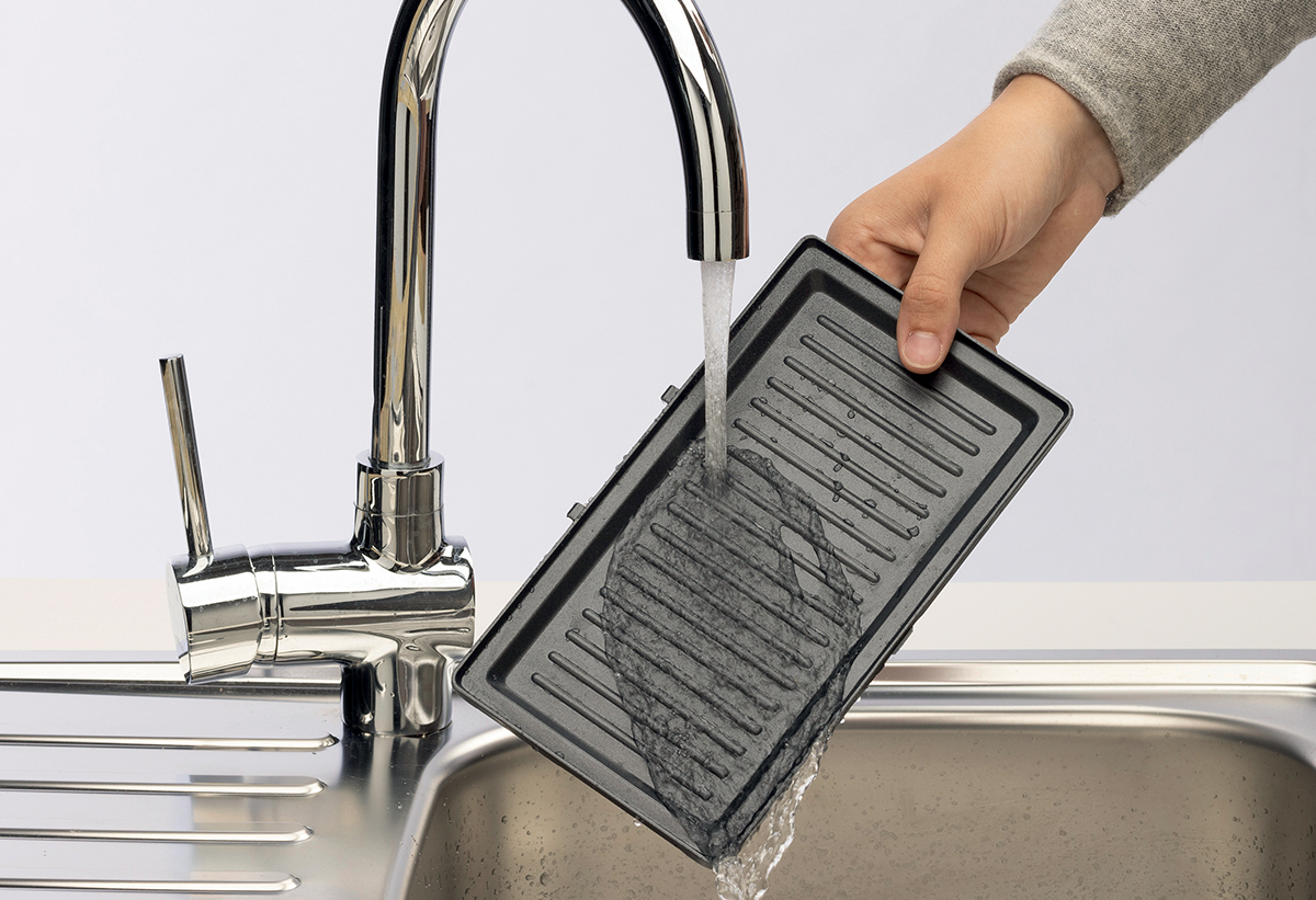 Απεικονίζεται το χέρι ενός άντρα να ξεπλένει με νερό την αποσπώμενη σχάρα. 